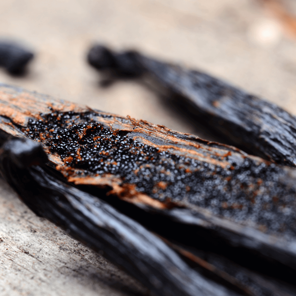 Split vanilla beans close-up with dark interior and black seeds on rustic wooden surface