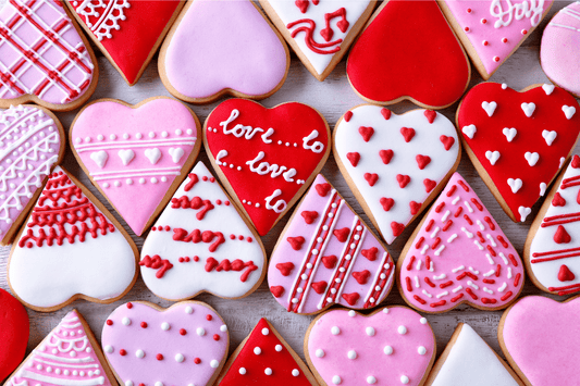 Heart-shaped cookies with vibrant icing are arranged in various shades of red, pink, and white. Decorative patterns and "love" messages convey a romantic vibe.