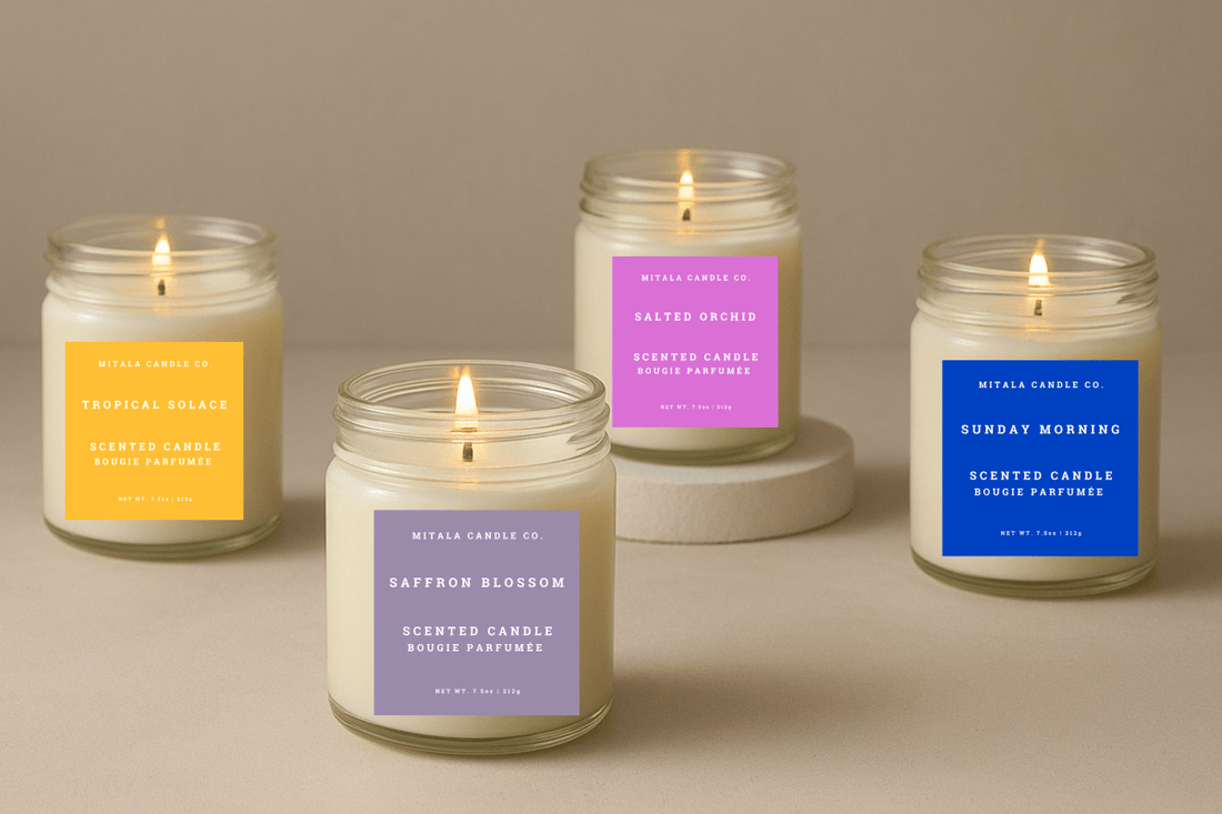 Four scented Mitala Candle Co. candles in jars with vibrant labels, lit and arranged on a neutral surface, creating a cozy ambiance.