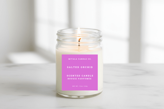 A clear glass soy candle jar with a soft glowing flame on a marble surface, candle safety tips from Mitala Candle Co.