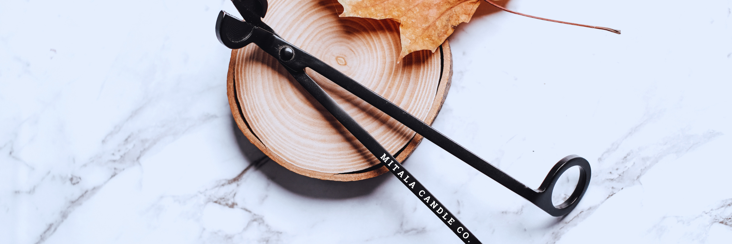 black Candle trimmer on wooden circle block and dry leaf on a marble counter