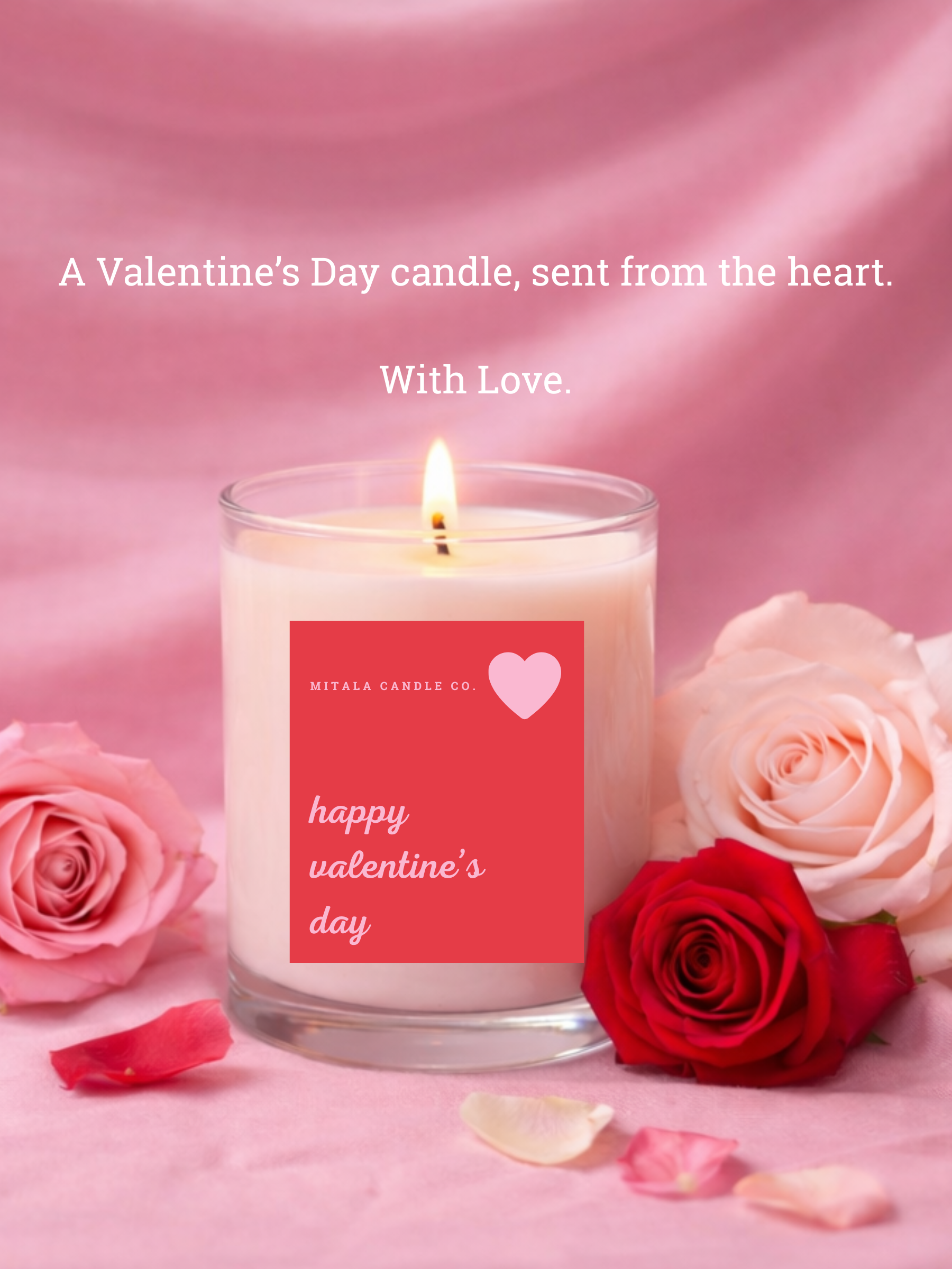 A lit Mitala Candle Co.  candle in a glass jar with "Happy Valentine's Day" label, surrounded by pink and red roses on a soft pink fabric, creating a romantic feel.