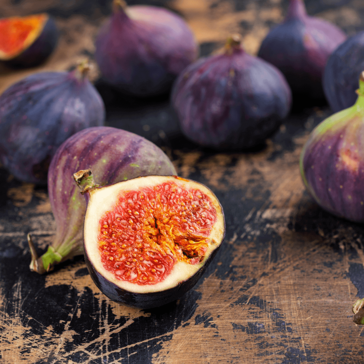 Close-up of fresh figs on rustic wooden surface, with one fig cut open to reveal juicy red interior, creating an earthy tone
