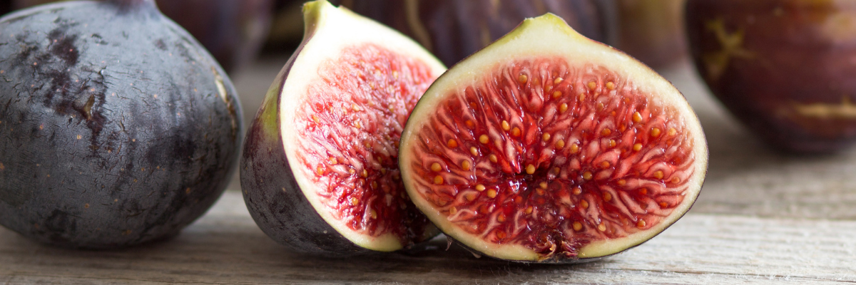 Close-up of fresh figs on wooden table, with two halves showing vibrant red interiors, creating a natural, wholesome feel