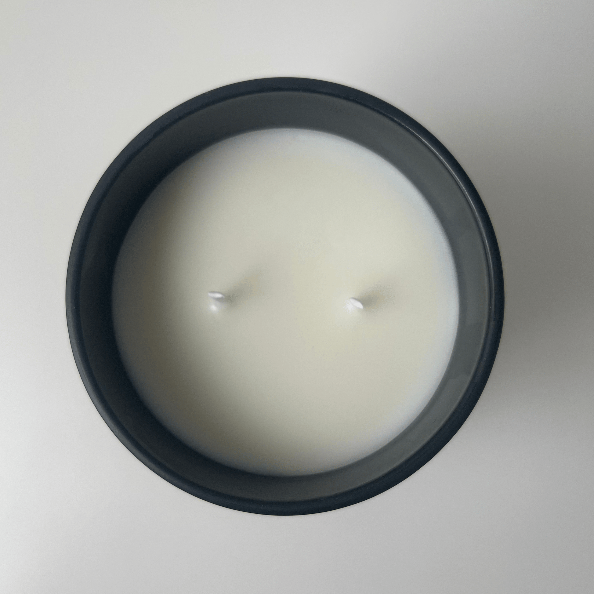 Top view of a Mitala Candle Co. sleek black candle jar filled with creamy white wax, featuring double wicks at the center against a light background.