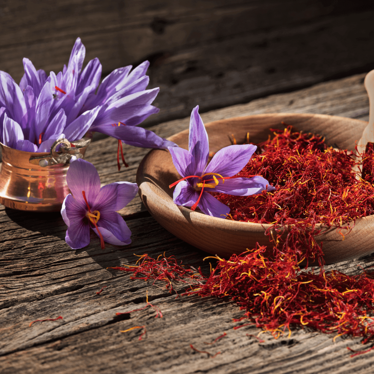 Purple saffron flowers and red saffron threads on rustic wooden table with wooden bowl holding vibrant saffron, conveying warm earthy feel