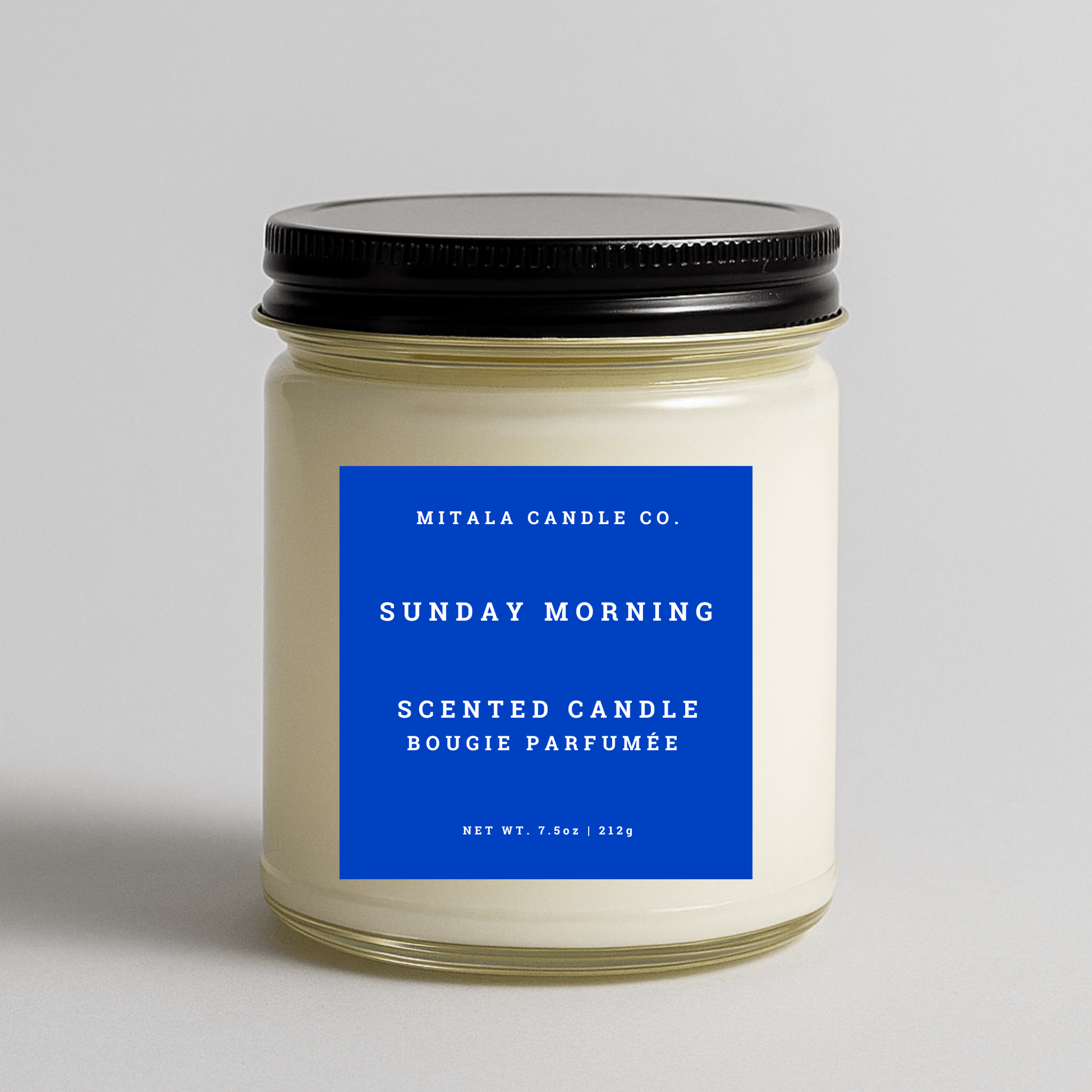 Mitala Candle Co. Sunday Morning scented candle with blue label and black lid, 7.5oz, on gray background