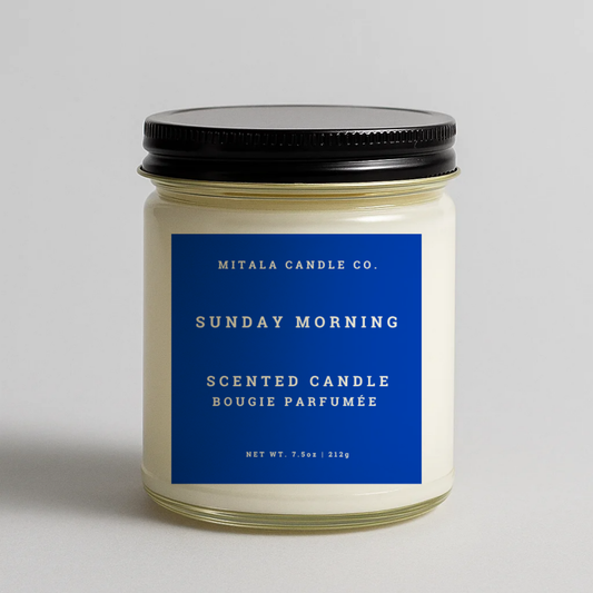 Mitala Candle Co. Sunday Morning scented candle with blue label and black lid, 7.5oz, on gray background